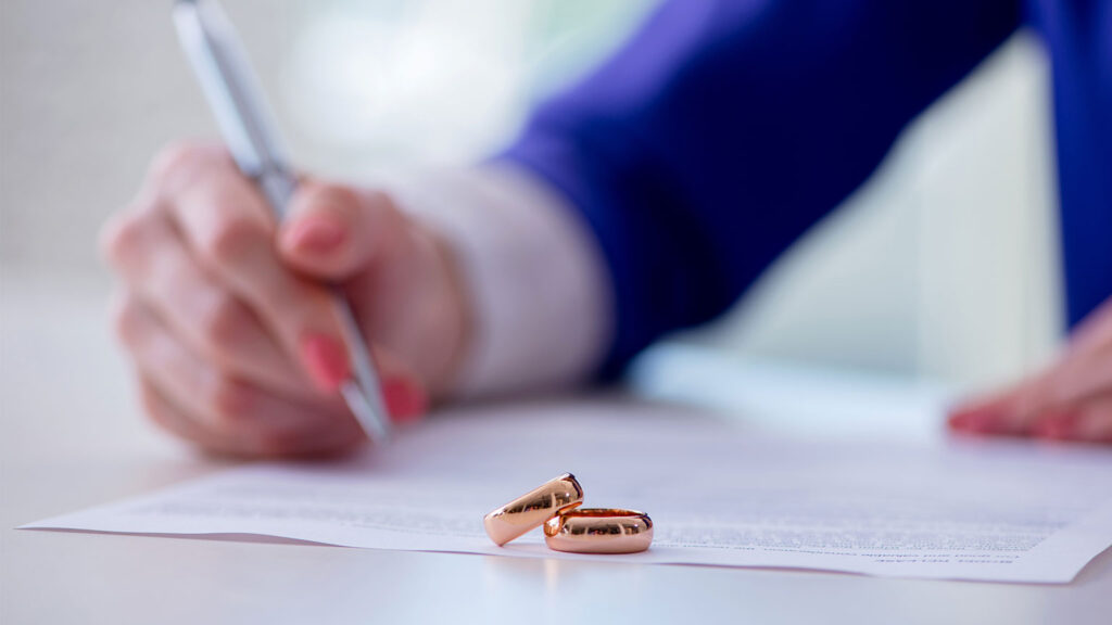person signing documents with two rings stacked on each other in the foreground.