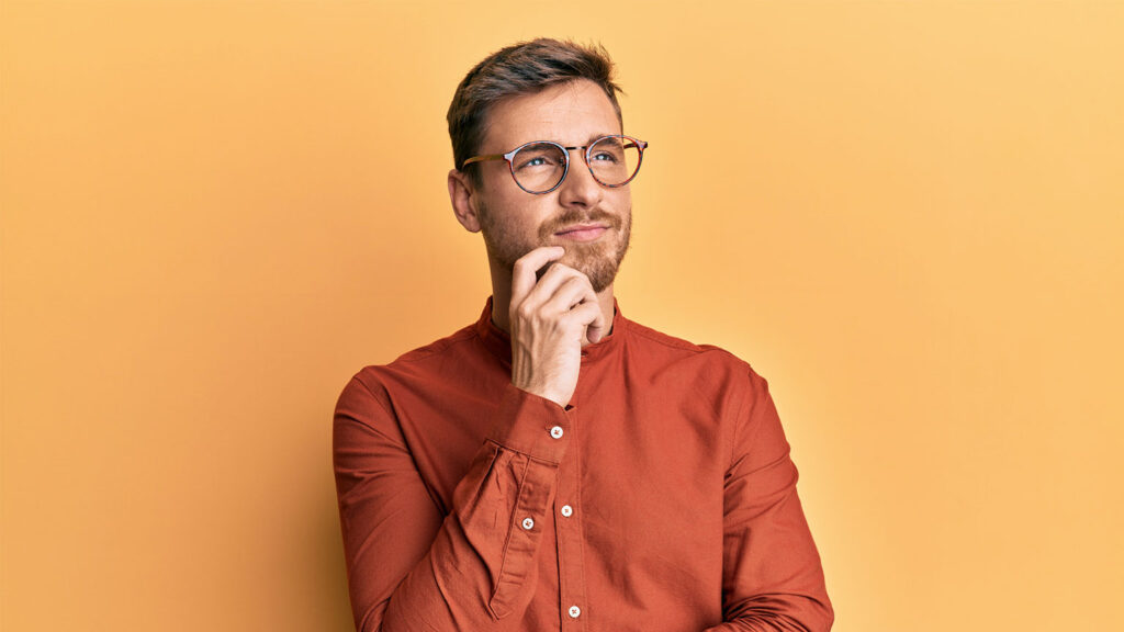 Man with glasses pondering something with hand scratching beard