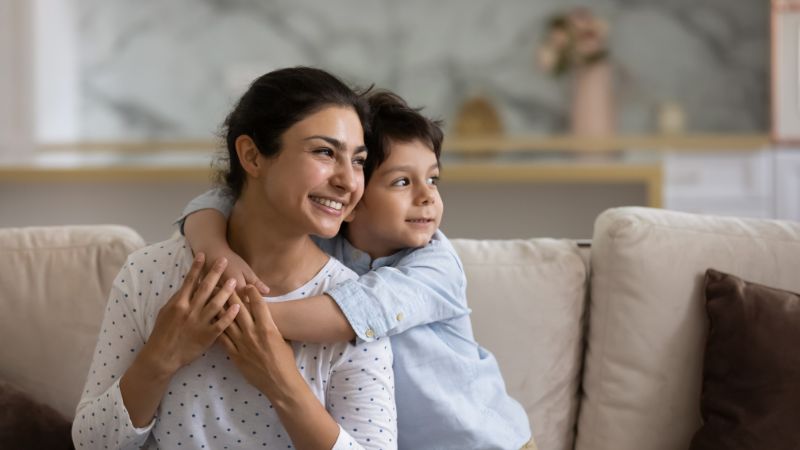 Mother sitting on couch while her son hugs her