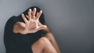 a woman in a black shirt hiding her head in one hand while putting the other hand up indicating "stop".